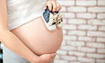 Pregnant woman holding small shoes on her naked belly