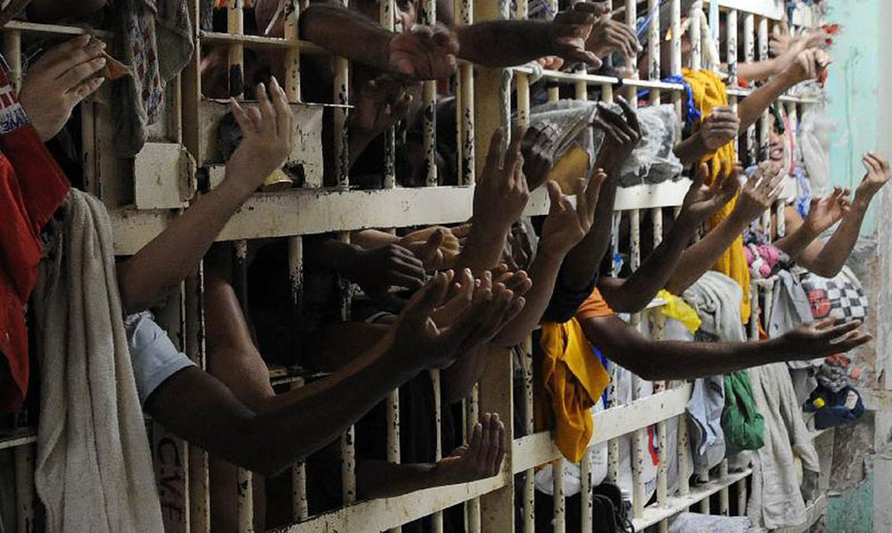 Photo of a cell full of men. We can see only arms and clothes stretched out between the bars.